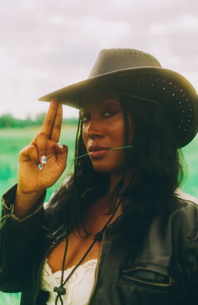 Stylish woman wearing a cowboy hat in a green field.