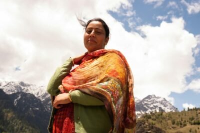 Woman in traditional attire with vibrant scarf against snowy mountains and blue sky.