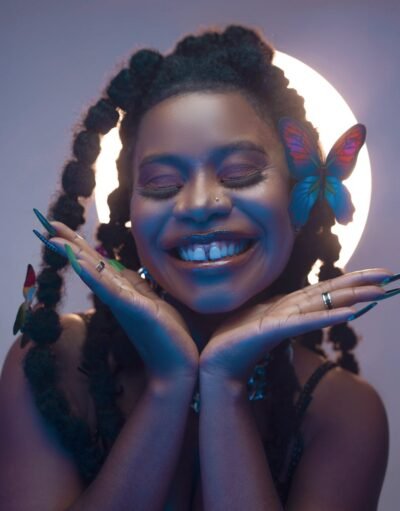 Captivating portrait of a joyful woman with braided hair and a butterfly accessory, embracing nature's beauty.